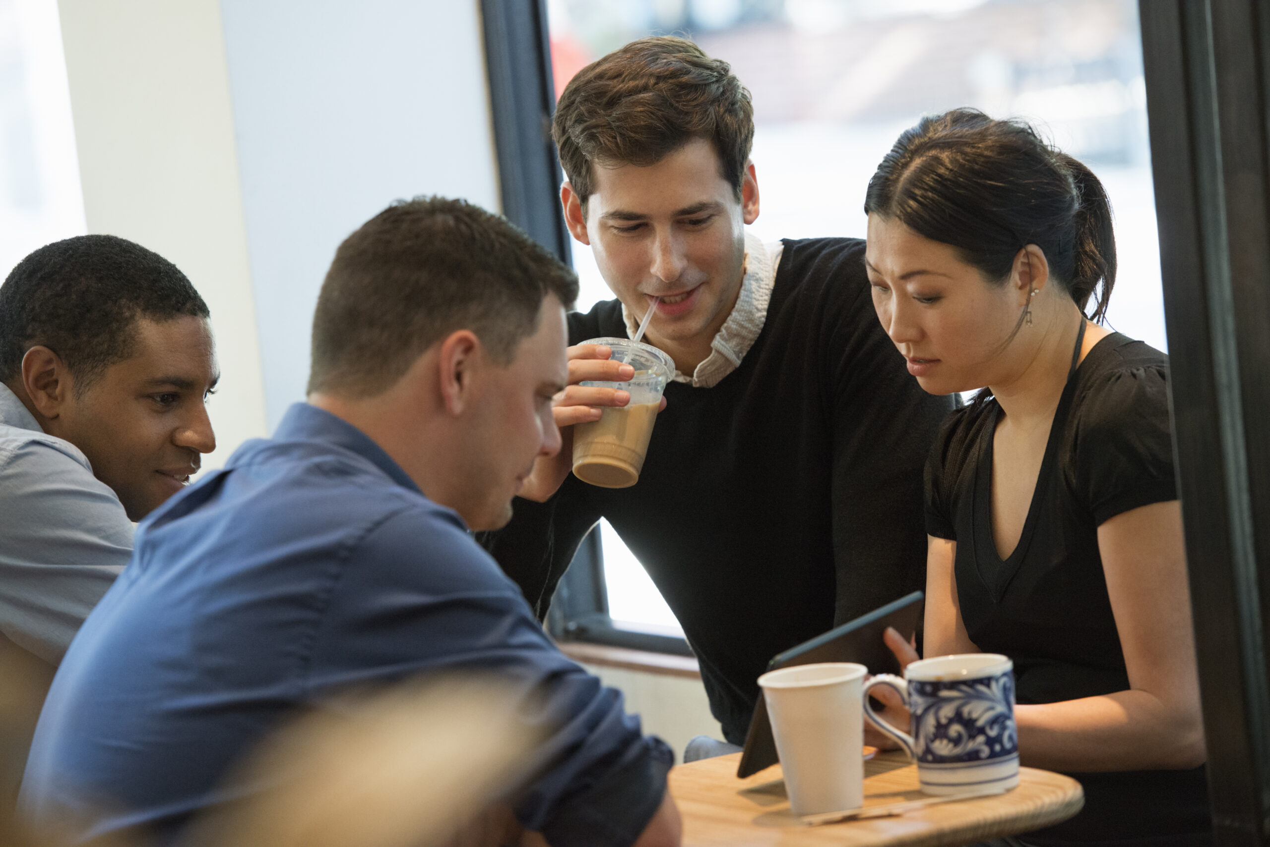 Business Casual,USA,A group of people sitting around a table in a coffee shop. Looking at the screen of a digital tablet. Three men and a woman. customers talking about your brand